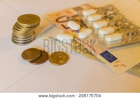 White Tabletts with euros banknotes and coins. Concept Pharmaceutical business cost of health medecine. Scattered pills.