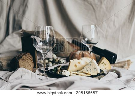 Two empty wineglasses are standing ready to be filled with dry red wine lying behind. Fresh bread, blue cheese, masdaam cheese and quail eggs are used as decoration. stylish shot