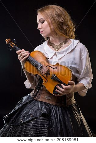Blond young girl looking at violin on black background