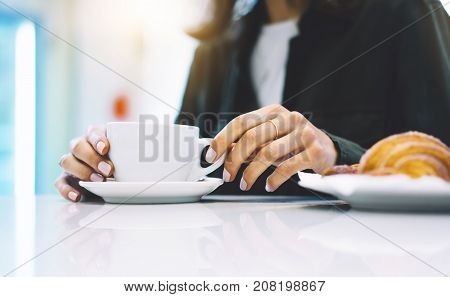 Young woman holding in female hands croissant and drink hot aroma coffee or tea in breakfast time hipster traveler smile girl communicate in the morning sun day holiday relax white cafe with friends