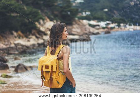 Back view hipster girl with backpack in sand coastline on nature landscape mock up. Traveler on background beach seascape and horizon mountain. Tourist look on blue sun ocean summer relax lifestyle