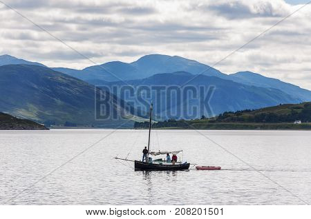Ullapool Scotland - August 15 2010: People in a small sailing boat in front of the small village of Ullapool in the Highlands in Scotland United Kingdom