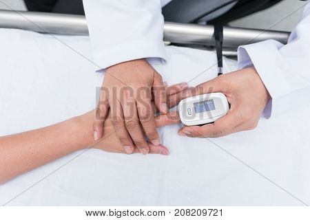 Doctor measuring blood oxygen levels of the sleeping elder patient on bed with oximeter.