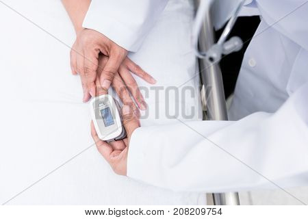 Doctor measuring blood oxygen levels of the sleeping elder patient on bed with oximeter.