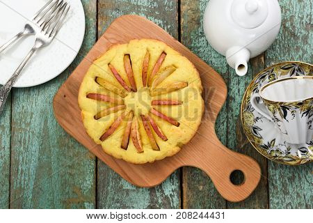 Homemade round cake with apple slices looking like sun rays with teaware on old wooden blue table above view