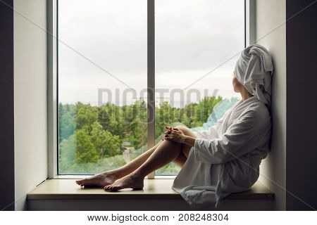 girl in a Bathrobe and towel on head sits on the window sill on the highest floor of the hotel
