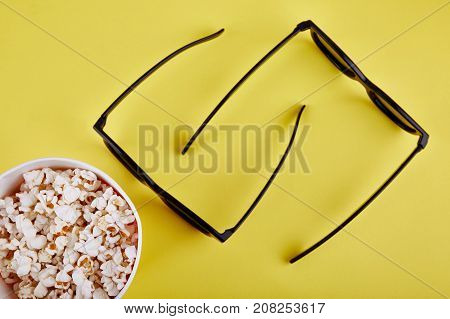 Bowl with popcorn and 3D glasses on a yellowbackground top view