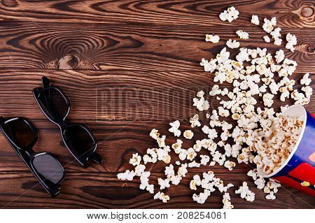 Bowl with scattered popcorn and pair 3D glasses on a wooden background