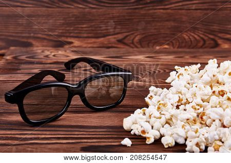 Bowl with scattered popcorn and 3D glasses on a wooden background