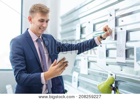 A young man in a blue suit makes notes in an office on a gray iron wall, on which are attached the magnet. Close-up.