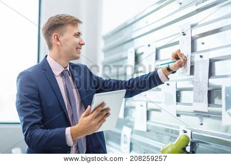 A young man in a blue suit makes notes in an office on a gray iron wall, on which are attached the magnet. Close-up.