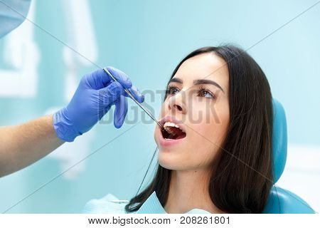 A dentist in purple gloves examines the teeth of a young pretty black-haired girl at his reception