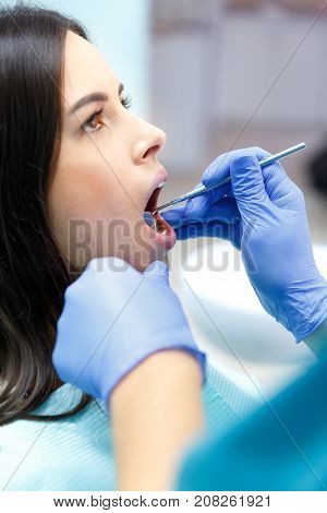 A dentist in purple gloves examines the teeth of a young pretty black-haired girl at his reception