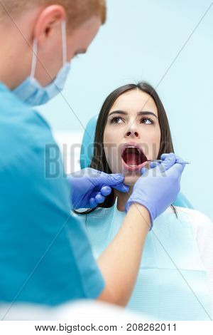 A dermatologist, a blonde man in purple gloves, examines the teeth of a young pretty black-haired girl at his reception