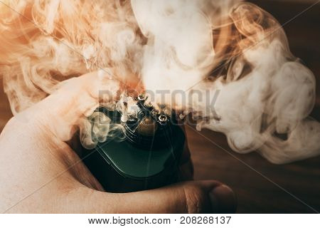 Clouds of vapor from RDA for vaping in man hand, modern vape electronic or ecig device, toned