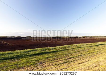 Industrial Field, Which Collects And Peat Processing. Photo Of Scenery. Peat Black Gathered In Large