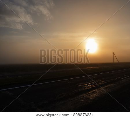 wet asphalt road, electric posts and fog during the sunrise. orange from a sunlight. landscape with poor visibility in the haze