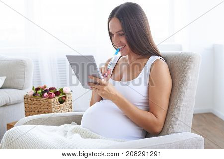 Closeup of delightful pregnant woman with pen holding jotter