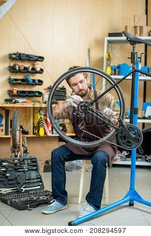 Master of repair in uniform sitting on chair and fixing wheel gear