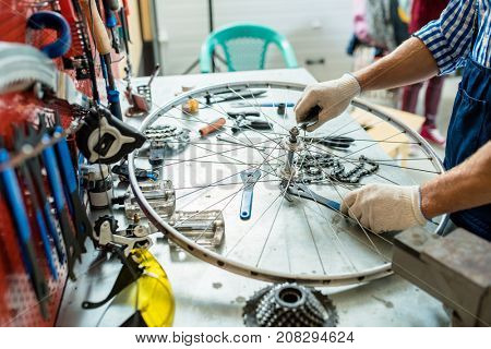 Gloved hands of repairing master tightening bolts on wheel by workplace