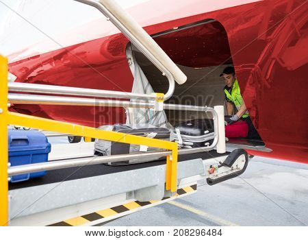 Worker Placing Baggage On Conveyor While Unloading Airplane