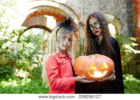 Little friends in halloween attire sharing jack-o-lantern at carnival party