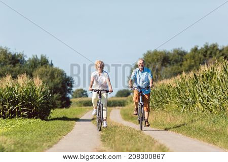 Full length of a senior active couple smiling and looking forward with confidence and serenity while riding bicycles in the countryside in summer