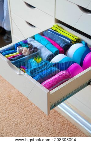 Neatly folded clothes with accessories in chest of drawers