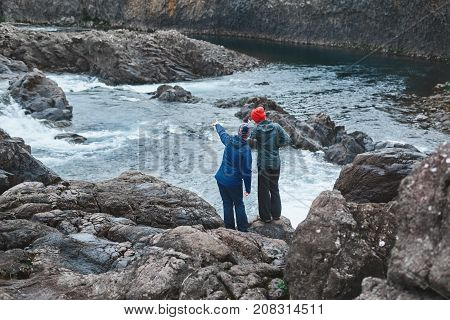 a women tourists in waterproof clothes stands on the Bank of the mountain river with small waterfall. Glanni waterfall, Iceland