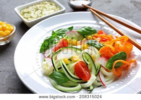 Plate with raw vegetable spaghetti and chopsticks on grunge background