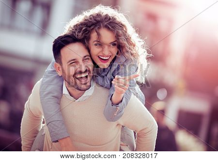 Man giving his pretty girlfriend a piggyback on a sunny day in the city.