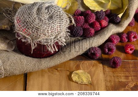 Raspberry jam and fresh raspberries on a wooden table in the garden