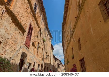Pienza, Italy - May 27, 2017: Beautiful narrow street with sunlight and flowers in the small magical and old village of Pienza, Val D'Orcia Tuscany.