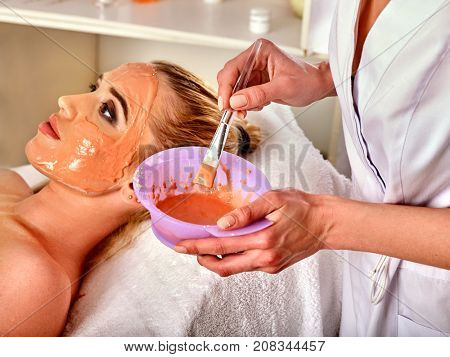 Collagen face mask. Facial skin treatment. Woman receiving cosmetic procedure in beauty salon. Bottle with moisturizing cream on background. Removing black dots.