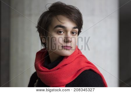 Dramatic Portrait Of Young Melancholy Woman In A Red Scarf Against Cocrete Wall. Concept Of Loneline