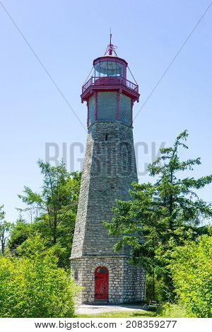 tall high stone lighthouse red door and top construction in park with grass trees on Toronto Island Intario Canada