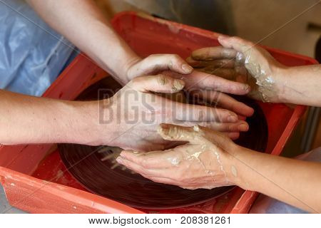 Hands of two people create pot on potter's wheel. Teaching pottery carftman's hands guiding