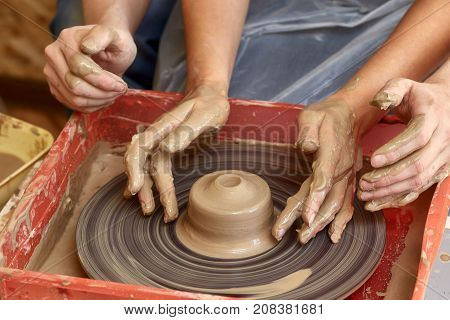 Hands of two people create pot on potter's wheel. Teaching pottery carftman's hands guiding