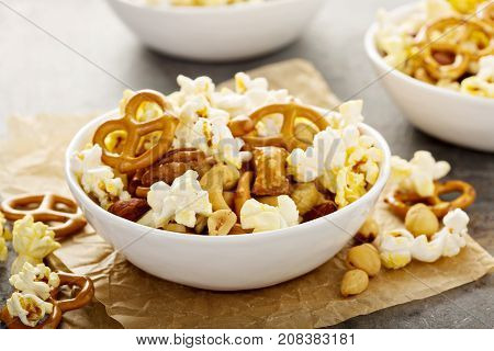 Homemade trail or snack mix with popcorn, pretzels and nuts in white bowls