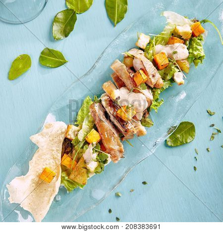 Menu of gastronomic restaurant. Warm salad with chicken baked pumpkin and cheese halumi with fresh herbs on  glass plate on  blue wooden table. Top View