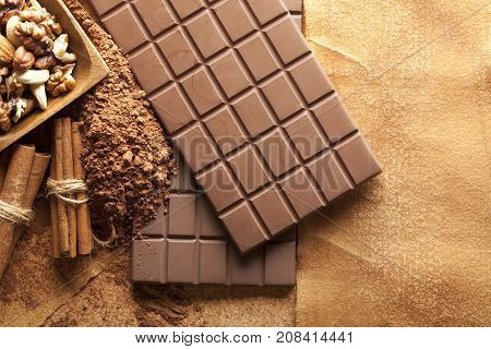 Four chocolate bars cinnamon sticks cocoa and mixed nuts in a bowl