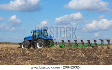 a large blue tractor plowing field against the beautiful sky. Work of agricultural machinery. Harvest