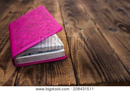 a closed pink bible on wooden background