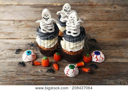 Halloween Cupcakes With Skeletons And Candies On Grey Wooden Table