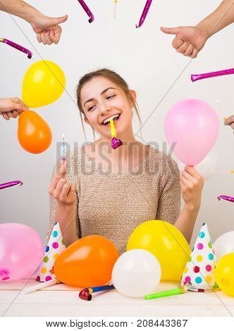 holidays, weekends, beauty concept. wonderful girl with charming smile with birthday whistle in her teeth, she is holding small pinl balloon and blue candle for cake