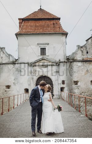 Beautiful Gorgeous Bride And Groom Kissing. Happy Wedding Couple Hugging And Embracing At Old Castle