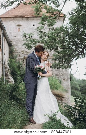 Beautiful Gorgeous Bride And Groom Walking In Sunny Park And Kissing. Happy Wedding Couple Hugging I