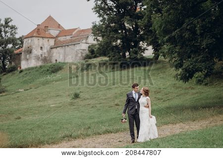Beautiful Gorgeous Bride And Groom Walking Outdoors. Happy Wedding Couple Hugging And Embracing At O