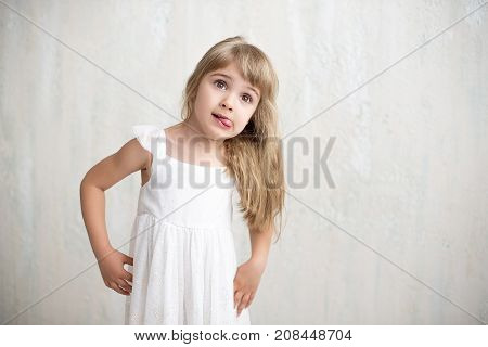 Portrait Of Pretty Little Girl In White Dress , She Is Smiling And Showing Tongue. She Is Happy And