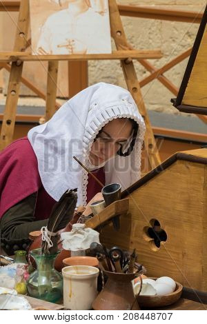 Medieval reenactor in scribe costume practicing traditional illumination writing calligraphy with feather quill and ink, Mdina, Malta, April 2017